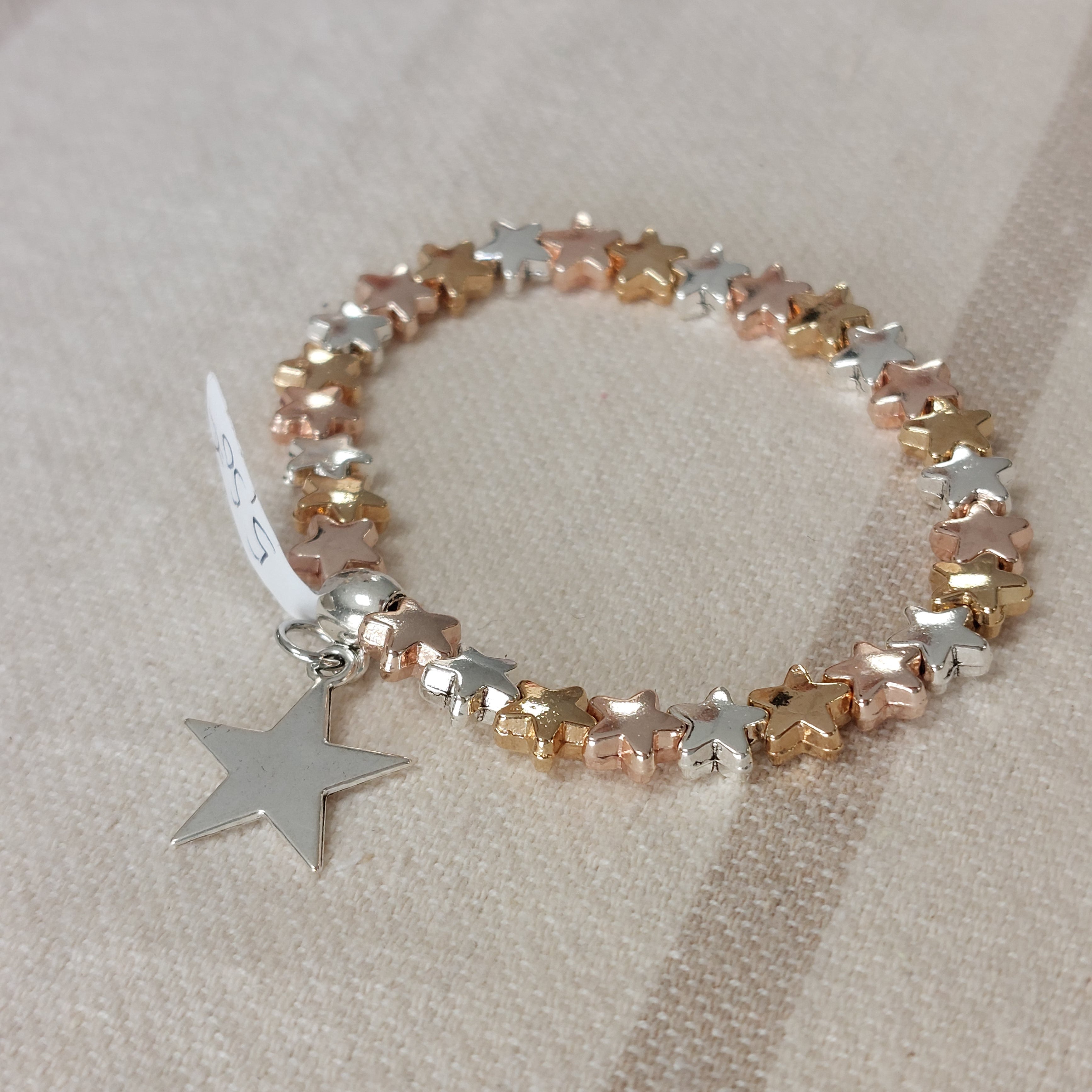 Bracelet élastiqué constitué de perles aciers en forme de petites étoiles bombées dorées et argentées et fini par une pampille aussi en forme d'étoile à cinq branches argent et plate sur carry le rouet