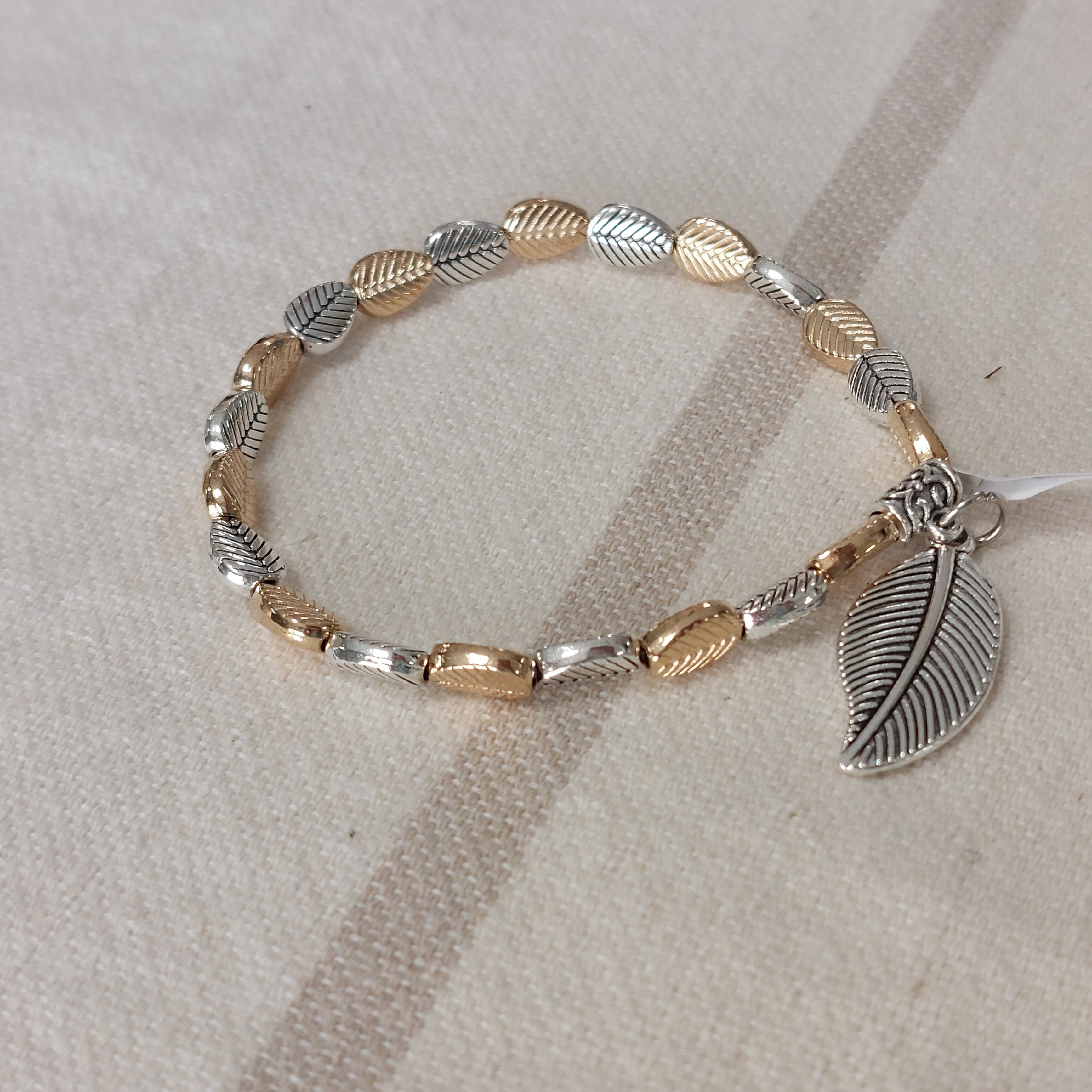 Bracelet élastiqué constitué de perles aciers en forme de petites feuilles dorées et argentées et fini par une pampille aussi en forme de feuille argent et rainurée sur martigues