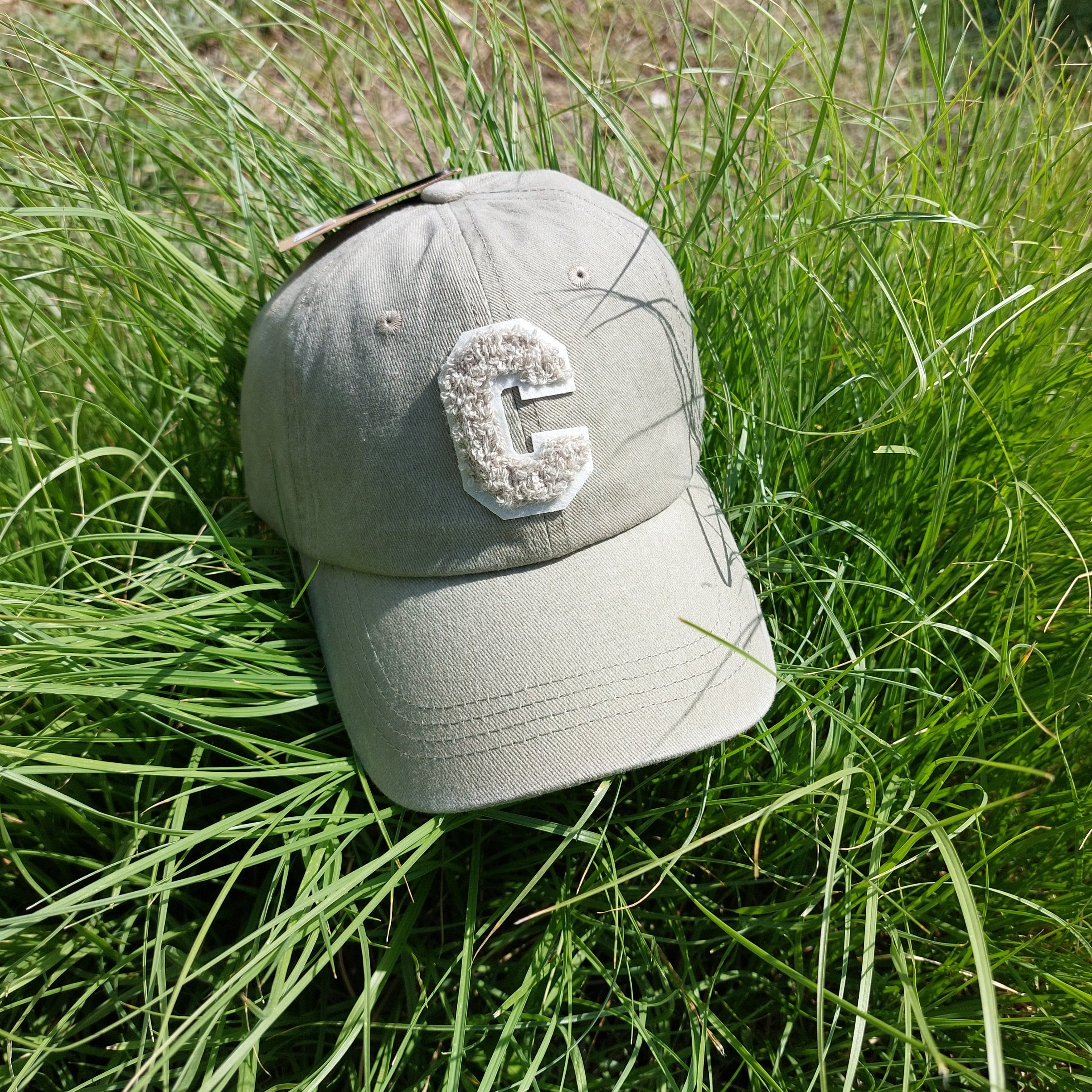 Casquette Ponteau est en tissus uni de forme base Ball coloris beige délavé, réglable par l'arrière elle a un C majuscule en moumoute sur le devant et une petite bille sur le dessus