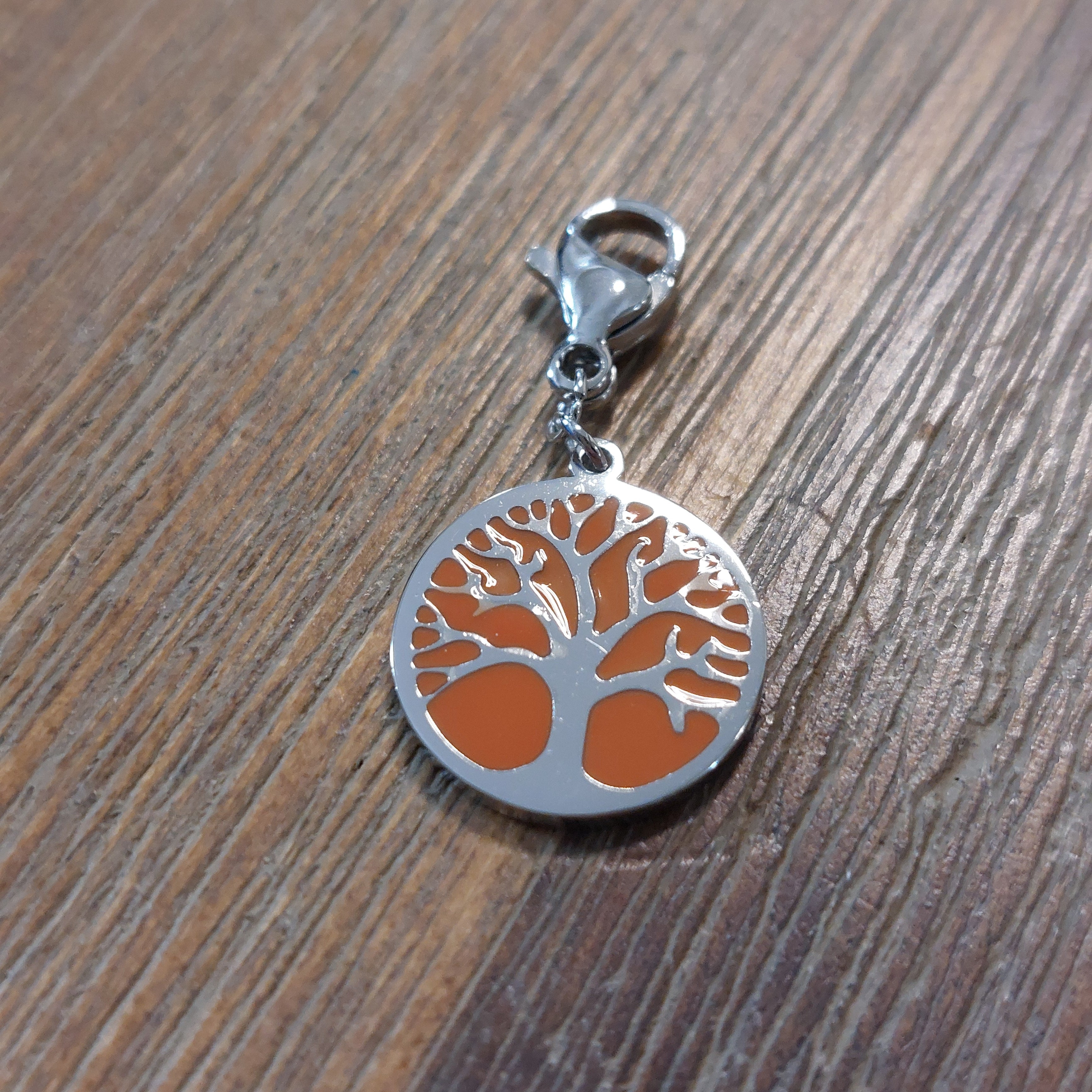 charm ou breloque avec un petit fermoir pour ajouter à un collier où à un bracelet en accumulation personnalisé. il represente une pastille ronde motif arbre de vie sur fond corail argent en acier inoxydable sur marignane