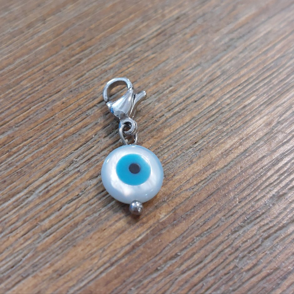 charm ou breloque avec un petit fermoir pour ajouter à un collier où à un bracelet en accumulation personnalisé. il represente un oeil de sainte lucie blanc centre bleu ciel en acier inoxydable sur carry le rouet
