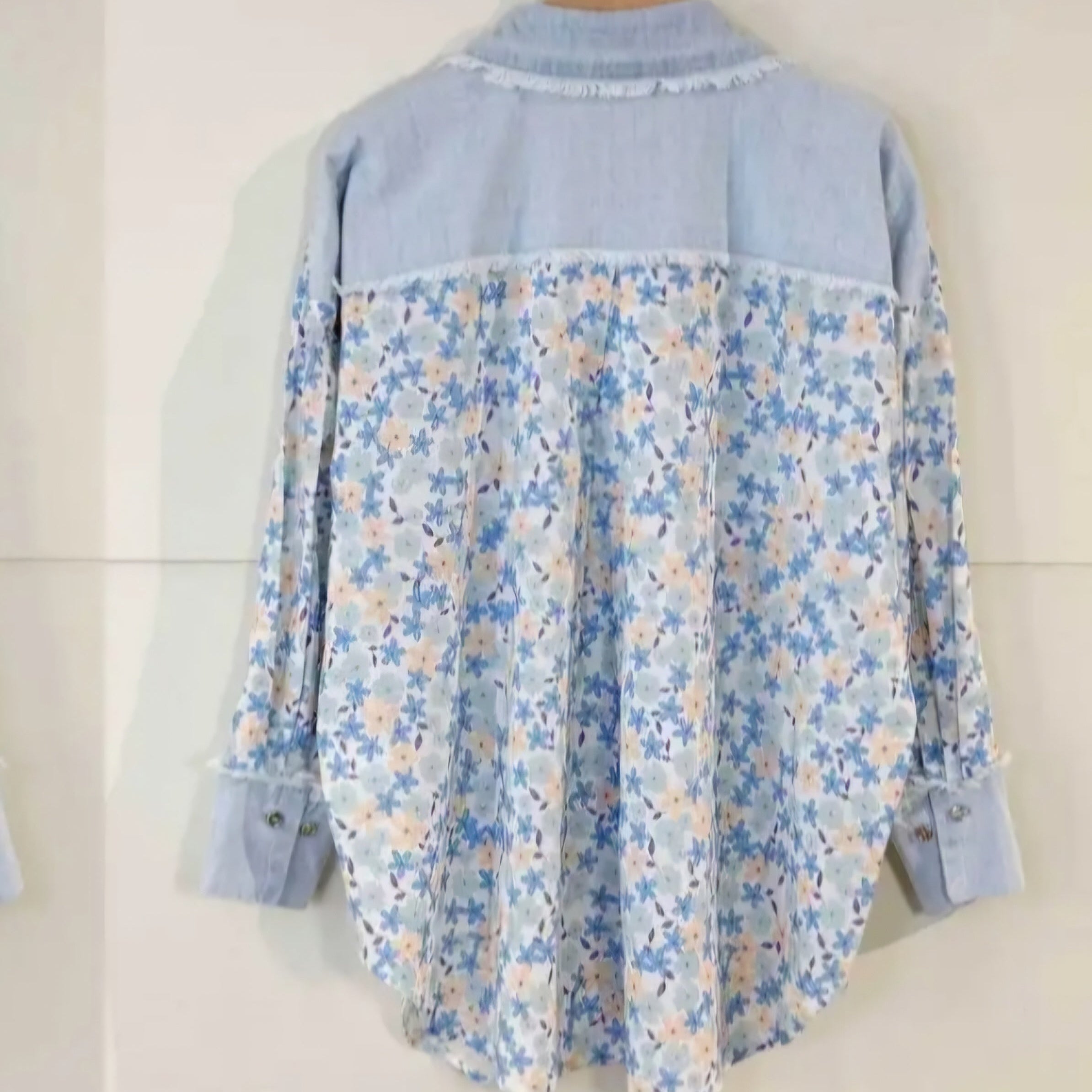 Chemise elina coupe droite manches longues au niveau des cuisses et arrondie sur les côtés. Elle est en popeline de coton imprimé petite fleur bleu ciel et beige sur fond blanc. Vue de dos dont le haut est en jean clair le col la couture boutonnée et les poignées sont aussi en jeans clair. Habillé du 36 au 42 sur Carry le rouet