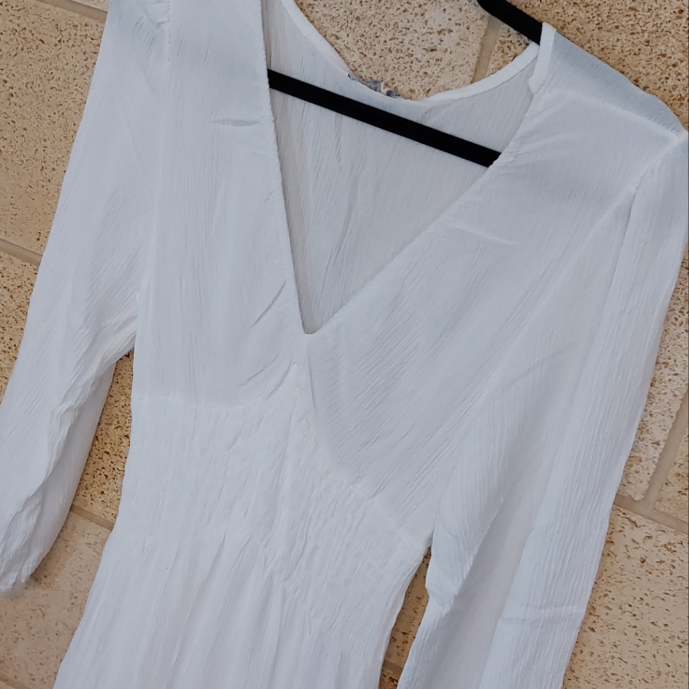 robe en crepon de viscose posé sur un ceintre. elle a un col env et des manches 3/4 fini par un elastique. smockée sous poitrine et taille elle possede une jupe ample t courte fini par deux volants. coloris blanc. carry le rouet
