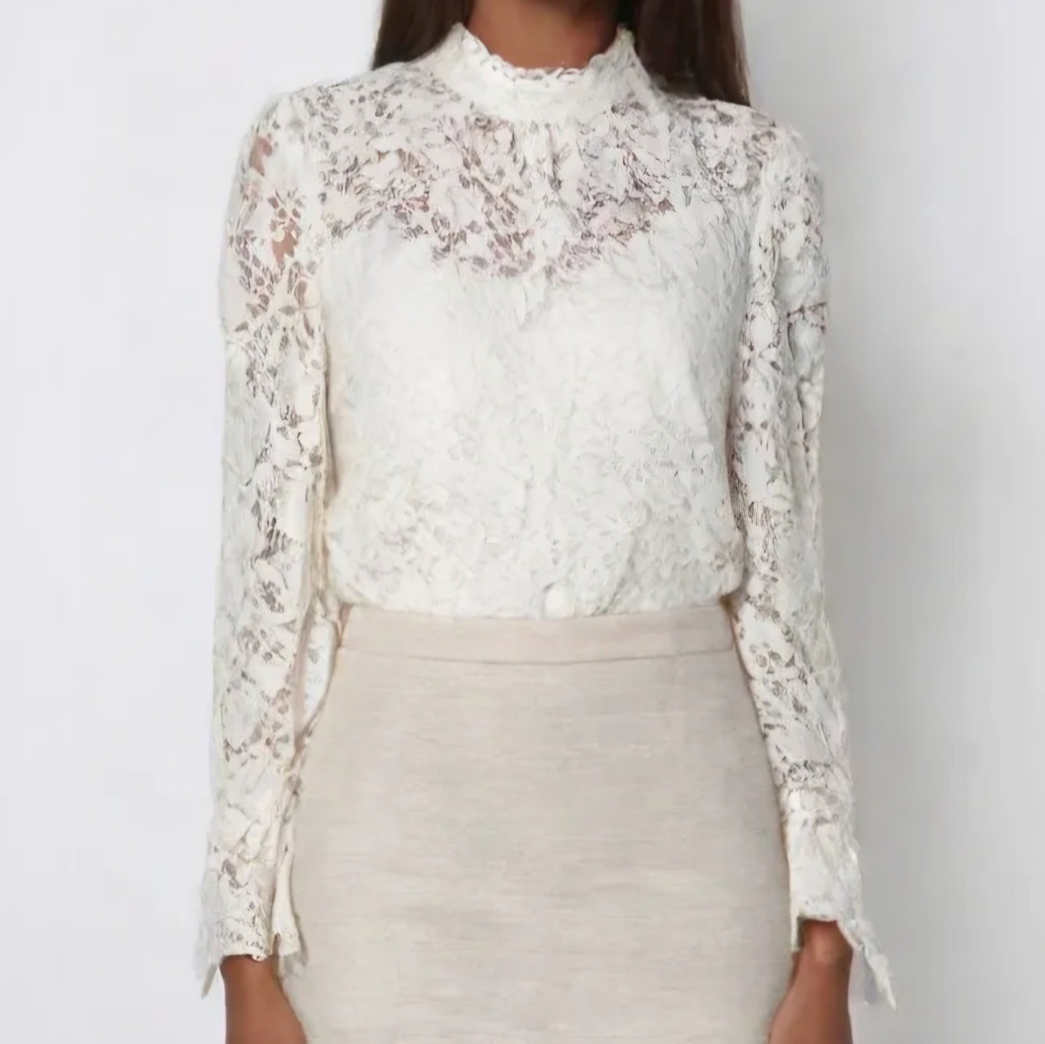 top en dentelle blanc col ras de coup legerement froncé pour l'aisance poitrine il a des manches longues tout en dentelles finis par une forme colombine et il est porté par une mannequin rentré dans une jupe droite taille haute sur carry le rouet