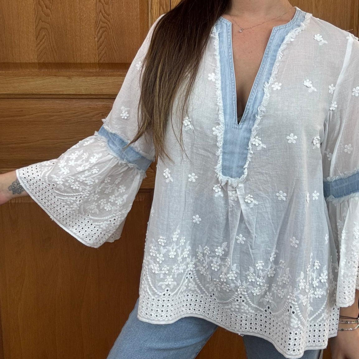 Top Faustine en taille s/m porté part ines qui porte du 36 et sur elle est plutôt ample. Col en v plongeant et bordé jeans clair elle arrive au niveau des cuisses, elle est en coton popeline blanche brodée de petite fleurs et broderie galon vague plutôt large sur le bas. Les manches ont un galon de 3 cm encerclant le coude en jean clair et deuxième partie de la manche forme colombine et toujours brodée. Style bohème chic