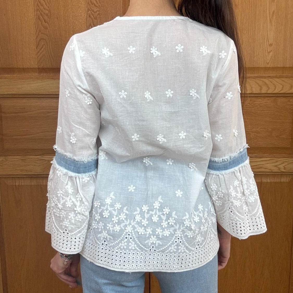 Top Faustine en taille s/m porté part ines qui porte du 36 et sur elle est plutôt ample vue de dos en coton popeline blanche brodée de petite fleurs et broderie galon vague plutôt large sur le bas. Les manches ont un galon de 3 cm encerclant le coude en jean clair et deuxième partie de la manche forme colombine et toujours brodée. Style bohème chic