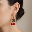 Boucles d’oreilles Soweto créoles acier inoxydable doré avec breloques papillons, perles colorées et cerises  bien rouges portées par une jeune femme 