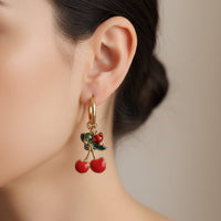 Boucles d’oreilles Soweto créoles acier inoxydable doré avec breloques papillons, perles colorées et cerises  bien rouges portées par une jeune femme 
