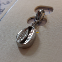 charm ou breloque avec un petit fermoir pour ajouter à un collier où à un bracelet en accumulation personnalisé. il represente un coqillage en acier inoxydable sur carry le rouet