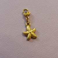 charm ou breloque avec un petit fermoir pour ajouter à un collier où à un bracelet en accumulation personnalisé. il represente une étoile de mer dorée en acier inoxydable sur carry le rouet 
