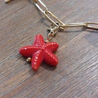 charm ou breloque avec un petit fermoir pour ajouter à un collier où à un bracelet en accumulation personnalisé. il represente une étoile de mer dodue et rouge en acier inoxydable sur aix en provence