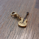 charm ou breloque avec un petit fermoir pour ajouter à un collier où à un bracelet en accumulation personnalisé. il represente une guitare dorée et détail des cordes en acier inoxydable sur enues la redonne