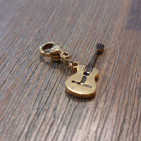 charm ou breloque avec un petit fermoir pour ajouter à un collier où à un bracelet en accumulation personnalisé. il represente une guitare dorée et détail des cordes en acier inoxydable sur enues la redonne