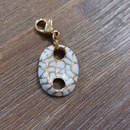 charm ou breloque avec un petit fermoir pour ajouter à un collier où à un bracelet en accumulation personnalisé. il represente un coquillage blanc et doré par des lézardes acier inoxydable sur aix en provence