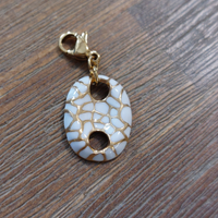 charm ou breloque avec un petit fermoir pour ajouter à un collier où à un bracelet en accumulation personnalisé. il represente un coquillage blanc et doré par des lézardes acier inoxydable sur aix en provence