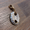 charm ou breloque avec un petit fermoir pour ajouter à un collier où à un bracelet en accumulation personnalisé. il represente un coquillage blanc et doré  en acier inoxydable sur martigues