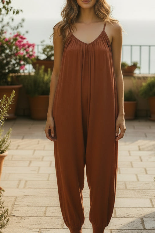 Combinaison longue Cléo terracotta portée en terrasse avec vue mer — col V, décolleté dos, bretelles fines, coupe loose, jambes resserrées à la cheville, 2 poches, taille unique 36/42 — ineva
