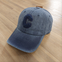 Casquette Ponteau est en tissus uni de forme base Ball coloris marine délavé, réglable par l'arrière elle a un c majuscule en moumoute blanche sur le devantet une petite ville sur le dessus