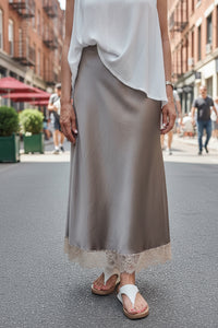 Jupe longue satin Diana taupe portée en ville avec top blanc et sandales blanches — taille élastique stretch, coupe évasée longueur cheville, bordure dentelle florale, taille unique 34/42 — ineva
