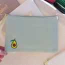 pochette en tissu matelasse de 14 cm sur 20 cm tissé vert d'eau avec un avocat brodé sur le coin bas gauche. fermeture zip sur le dessus sur carry le rouet