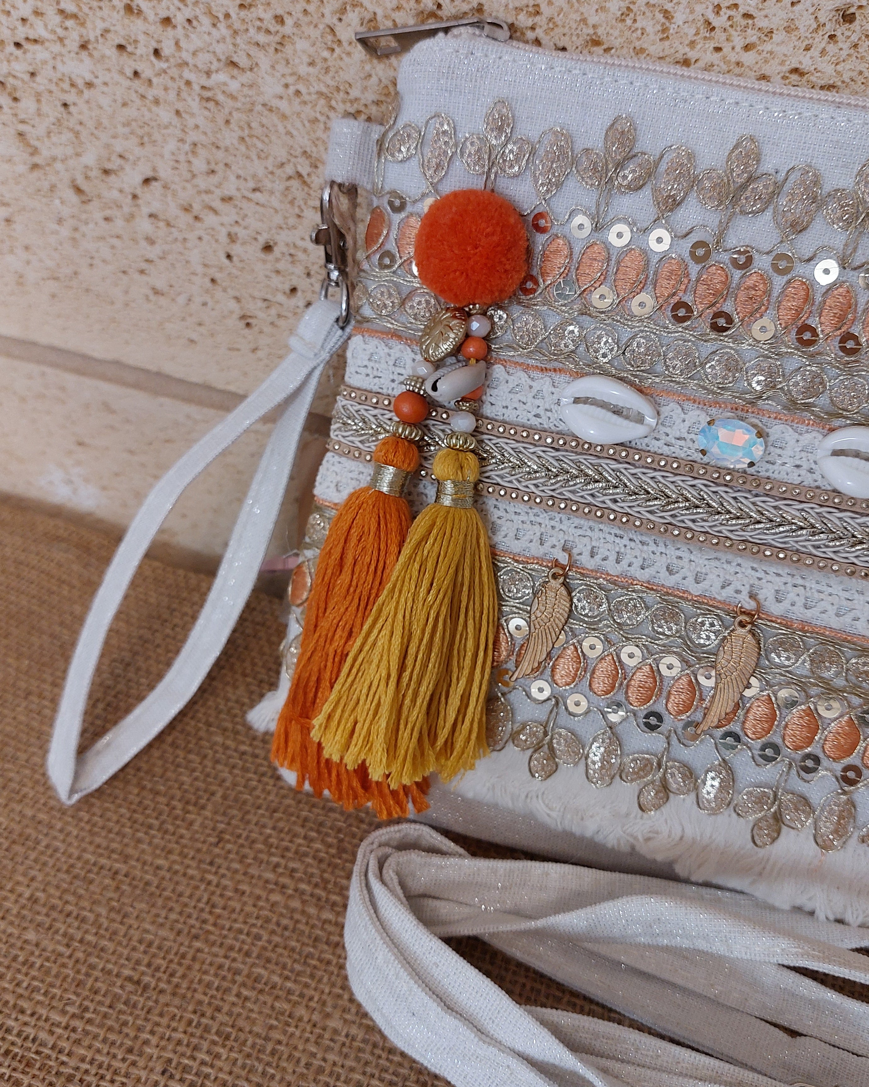 Détail broderies Pochette Nandi – pompons orange et moutarde, pom-pom feutré, sequins et perles sur fond blanc
