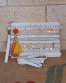 Pochette Nandi blanche brodée à plat – sequins dorés, pompons orange, coquillages et breloques plumes, bandoulière amovible
