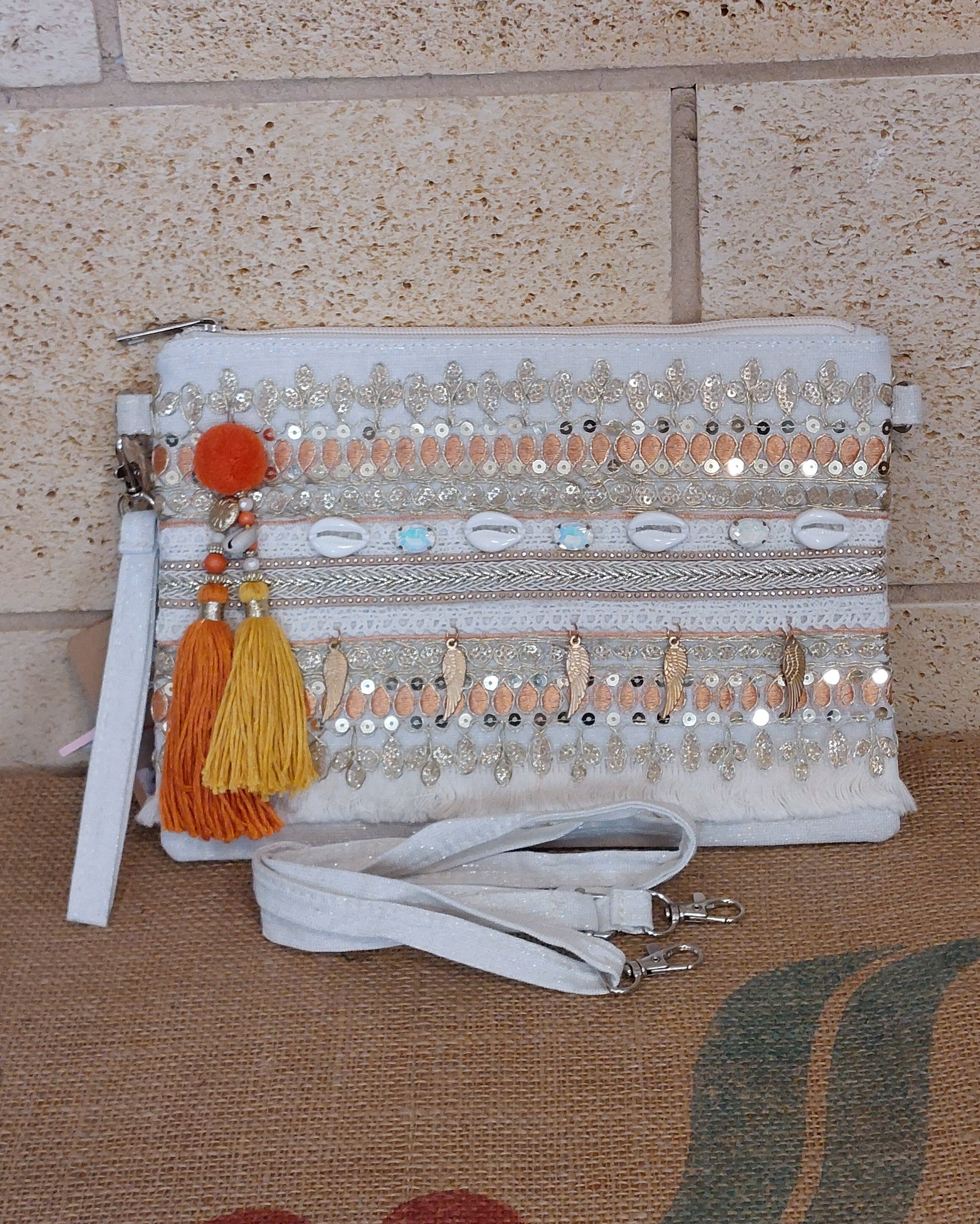 Pochette Nandi blanche brodée à plat – sequins dorés, pompons orange, coquillages et breloques plumes, bandoulière amovible
