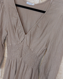 robe en crepon de viscose posé sur un ceintre. elle a un col env et des manches 3/4 fini par un elastique. smockée sous poitrine et taille elle possede une jupe ample t courte fini par deux volants. coloris camel. carry le rouet