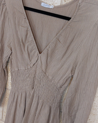 robe en crepon de viscose posé sur un ceintre. elle a un col env et des manches 3/4 fini par un elastique. smockée sous poitrine et taille elle possede une jupe ample t courte fini par deux volants. coloris camel. carry le rouet
