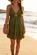 Robe courte volants étagés Nanou kaki portée sur la plage avec sac en osier et sandales lacées — col V, bretelles fines, broche soleil dorée amovible, Made in Italy — ineva
