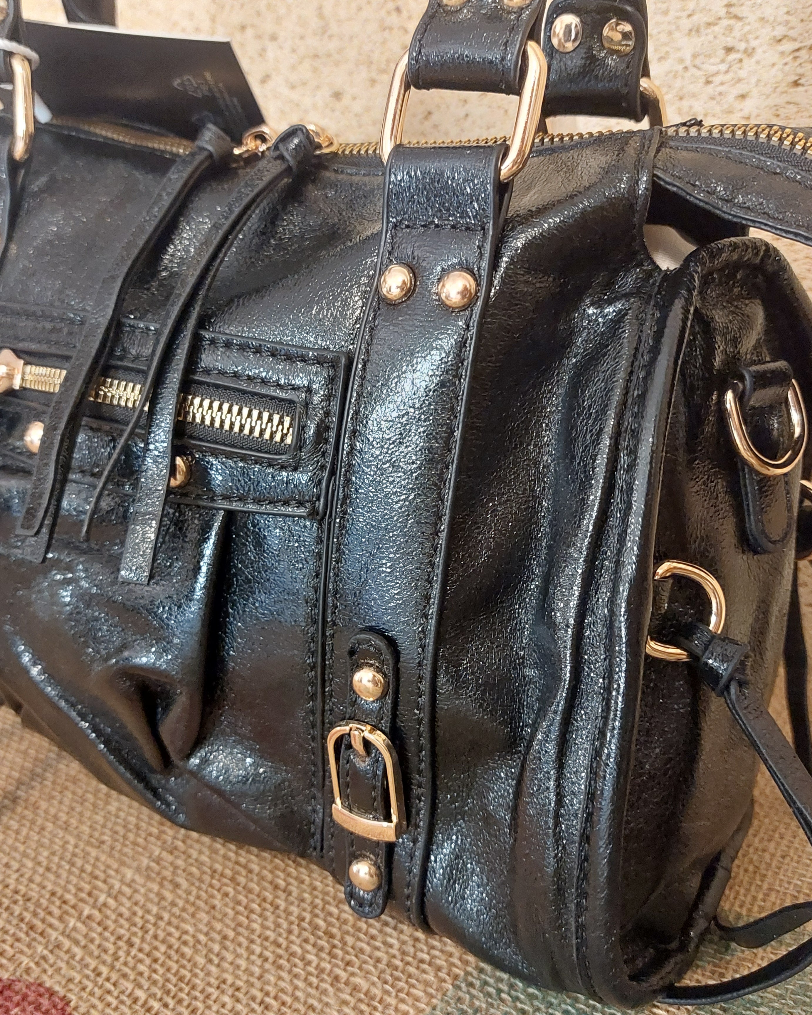 Détail du Sac Azilal simili cuir brillant métallisé noir — poche zip frontale cloutée, boucles dorées, lanières latérales, quincaillerie dorée — ineva

