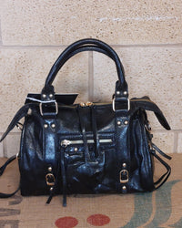 Sac Azilal simili cuir brillant métallisé noir vue de face — forme bowling, double poignée courte, poche zip frontale, clous et boucles dorés, 28x20 cm — ineva
