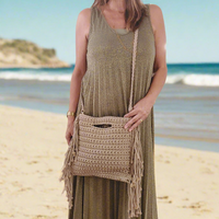 sac en maccramé porté  en bandoulière. Il possède des franges sur toute la longueur de chaque cotés, une poignée rectangle decoupée dans la matère sur le haut du cas et il  est en coloris camel sur mar gnane