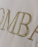 Gros plan broderie dorée BOMBASSE Tee-shirt Elsa – lettres sérifes fil doré métallisé sur coton blanc, finition haute qualité
