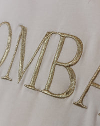Gros plan broderie dorée BOMBASSE Tee-shirt Elsa – lettres sérifes fil doré métallisé sur coton blanc, finition haute qualité
