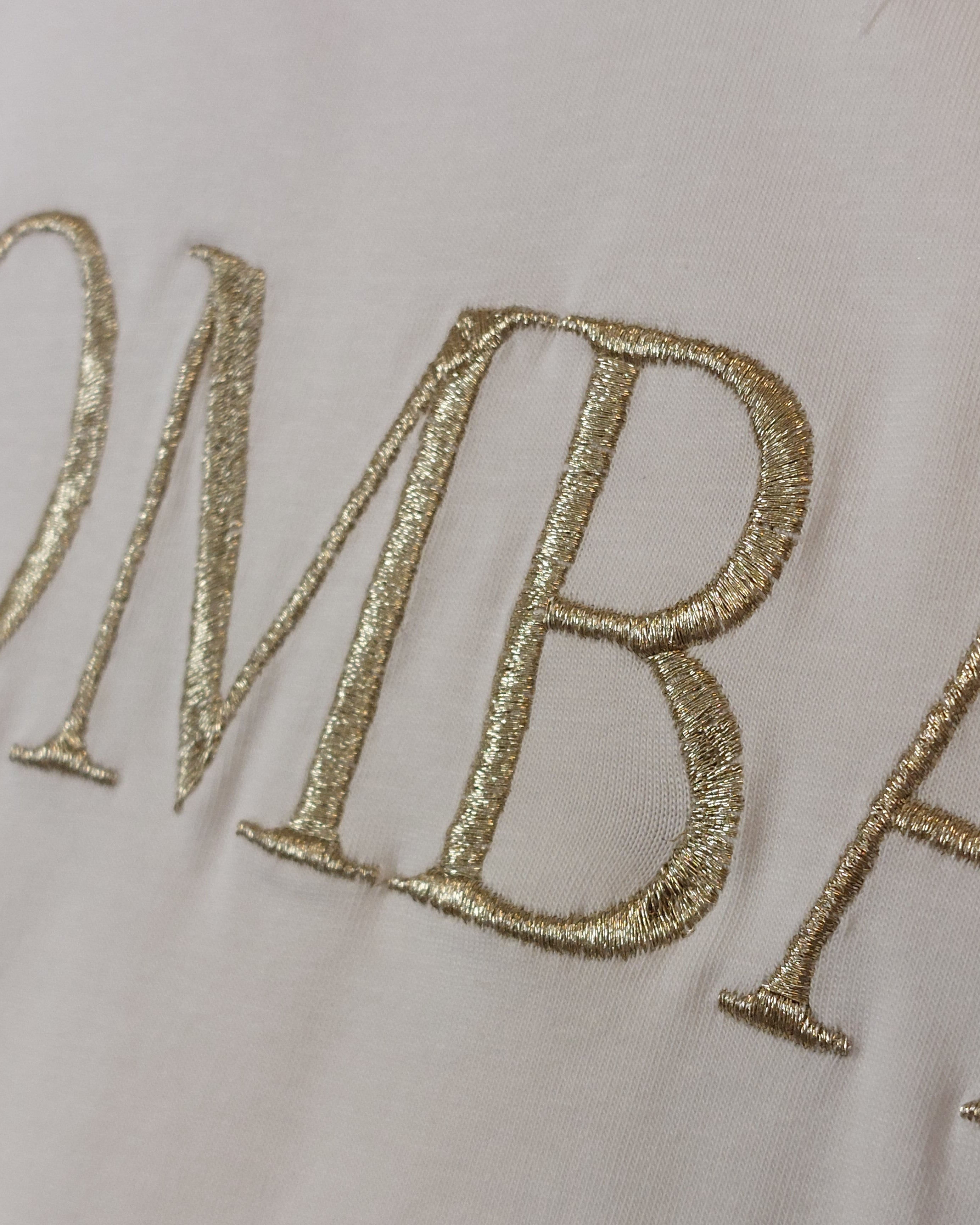 Gros plan broderie dorée BOMBASSE Tee-shirt Elsa – lettres sérifes fil doré métallisé sur coton blanc, finition haute qualité
