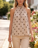 Top trapèze Charles beige à pois taupe porté en promenade – col halter à nouer, coupe fluide trapèze, voile polyester doublé, panier rotin, rue fleurie
