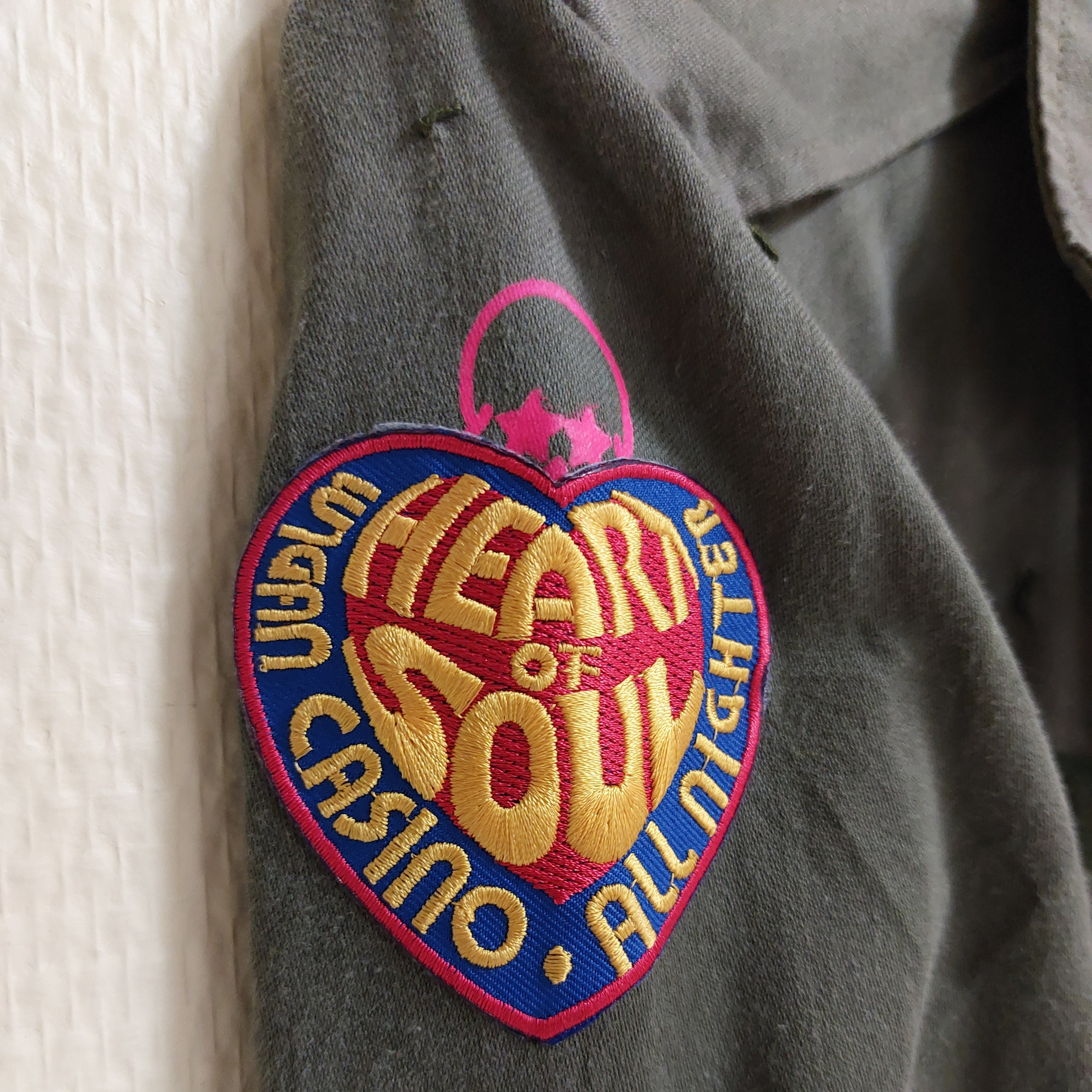 veritable veste mlitaire unie kaki. elle est customizée avec un patch brodé sur le haut de la manche droite au niveau de l'epaule representant un coeur avec inscription coloré sur Sausset les pins