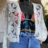 INEVA GILET EN COTON AJOURE BLANC ML- GILET COTON CROCHET  SUR CARRY le rouet il est porté sur un mannequin qui est vetu d'une jupe en jean et un haut de maillot de bain irisé